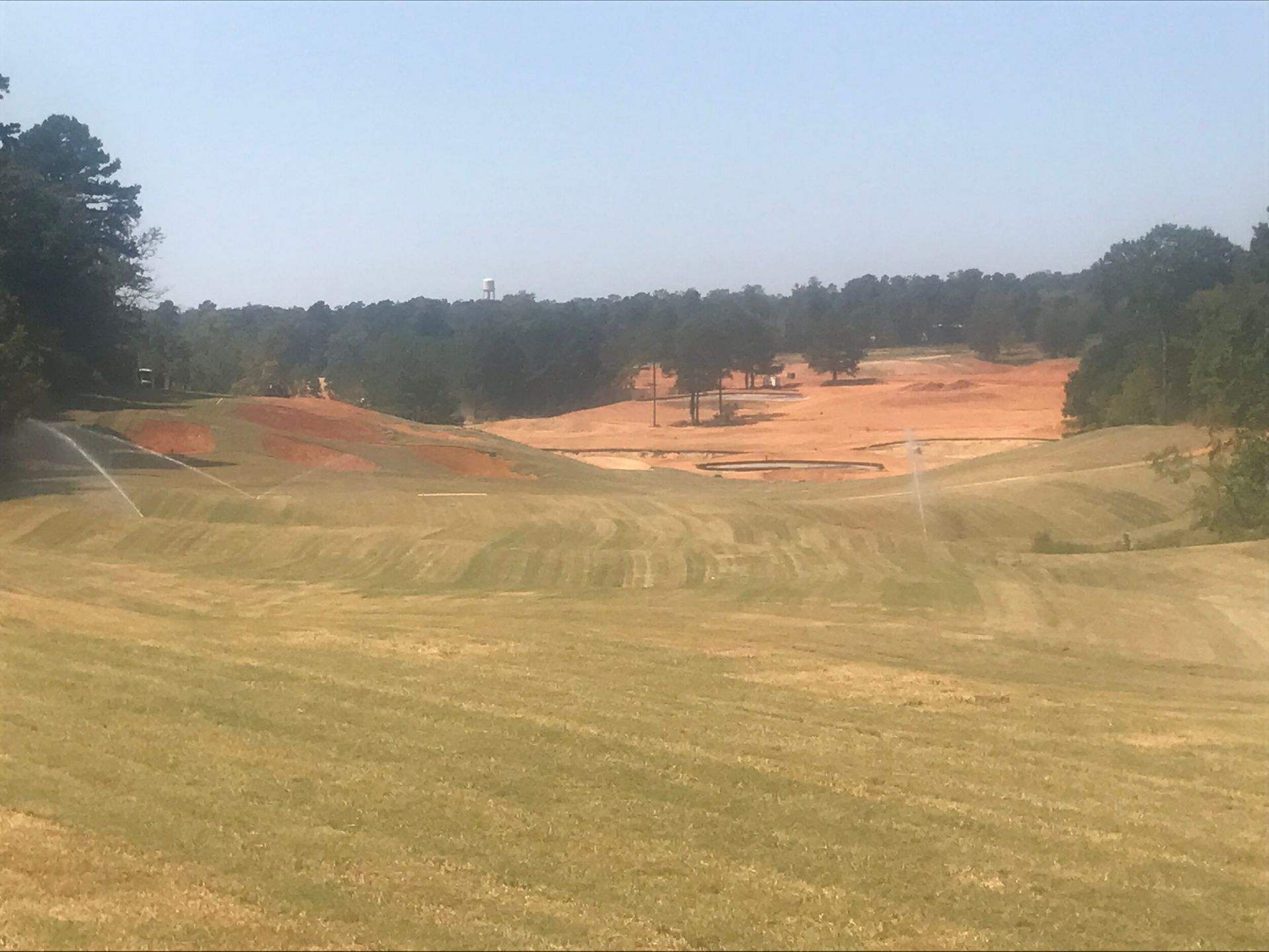 Grassy golf course fairway with sand traps and trees under a hazy sky
