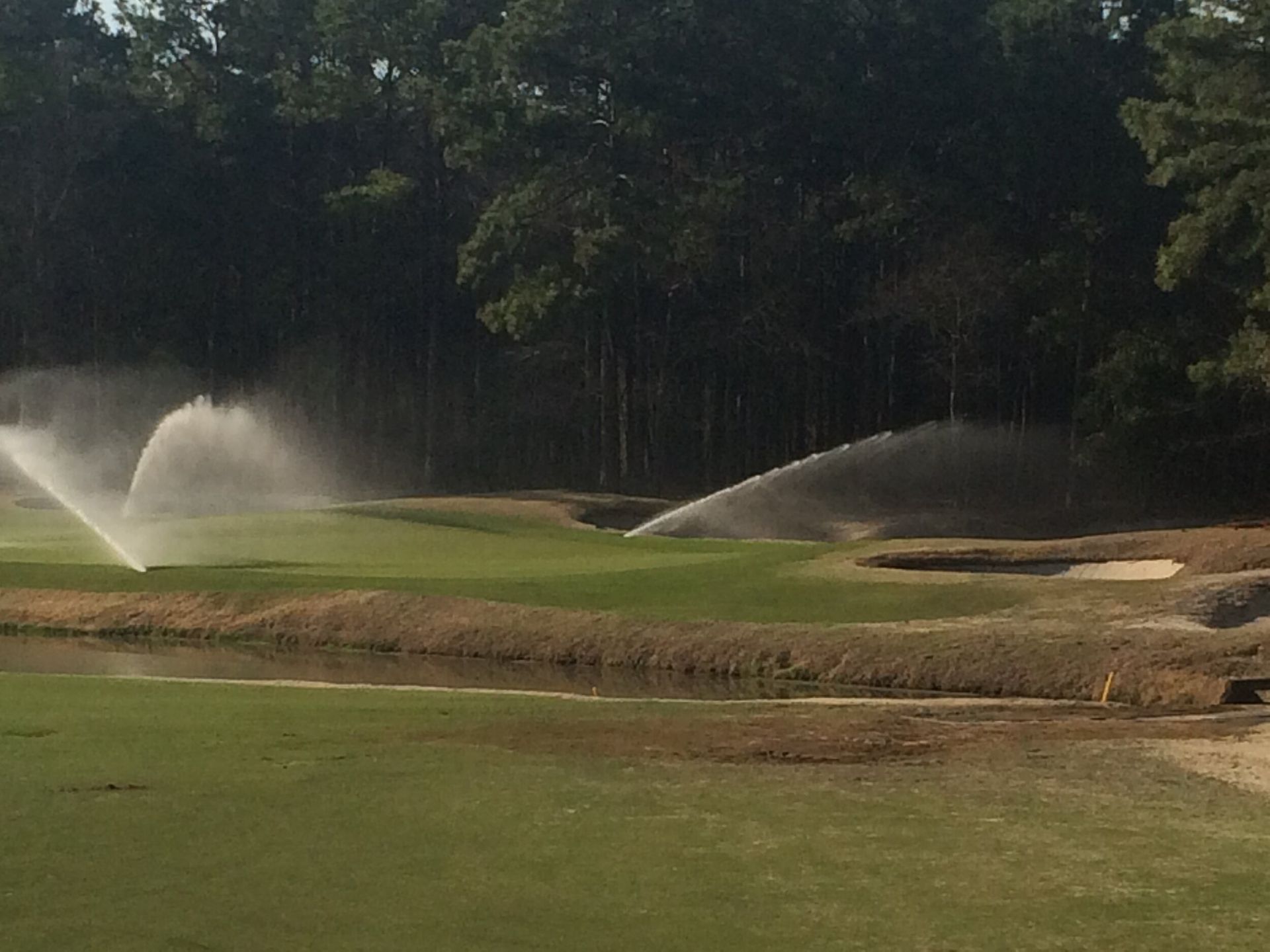 Golf course sprinkler systems watering a green with sand bunkers nearby
