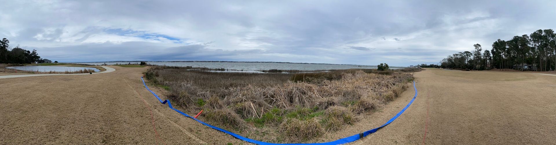 Wide sandy beach under cloudy sky with dune grass and distant coastline