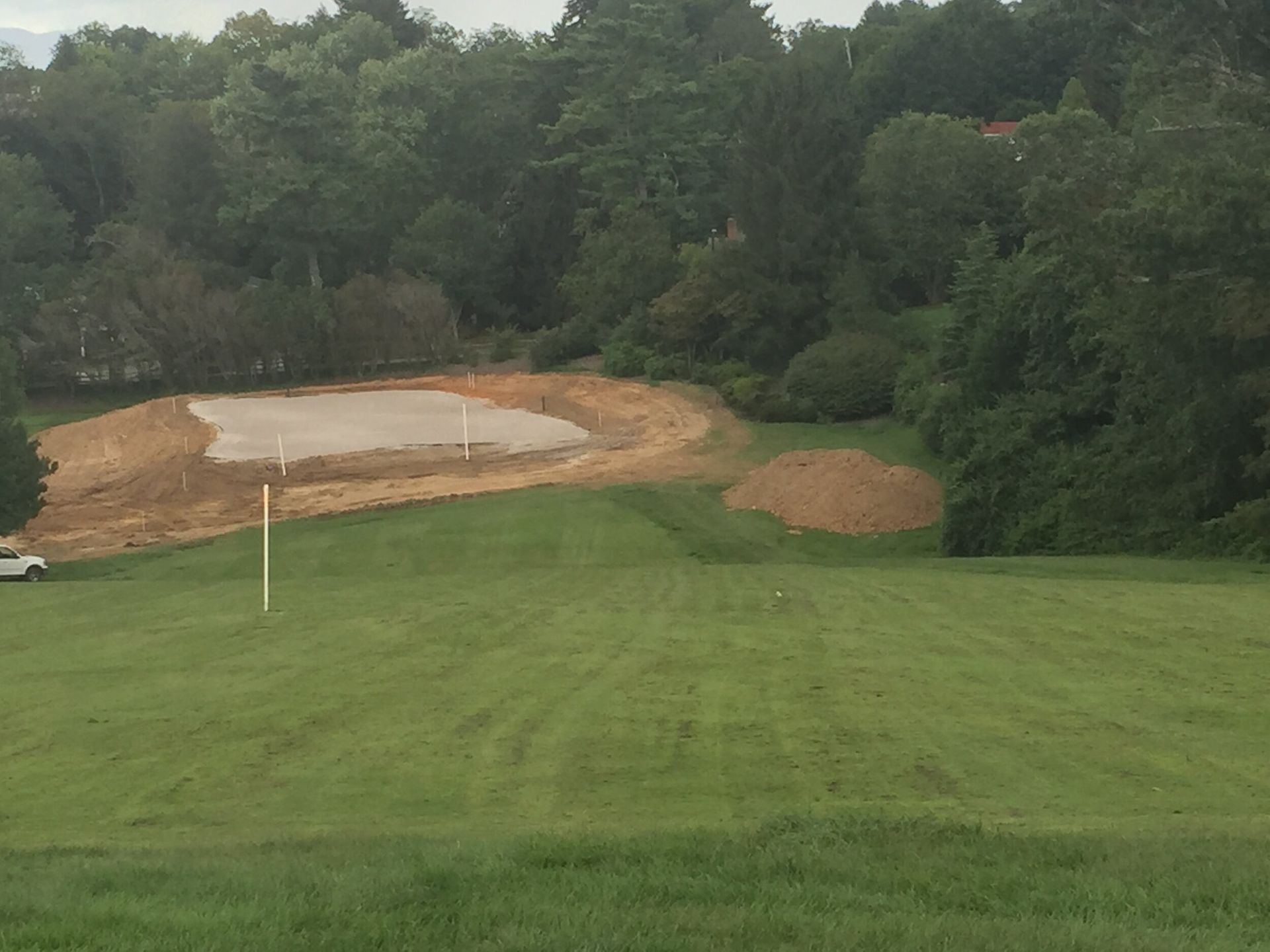 Golf course fairway overlooking a sandy, water-filled construction or repair area near trees