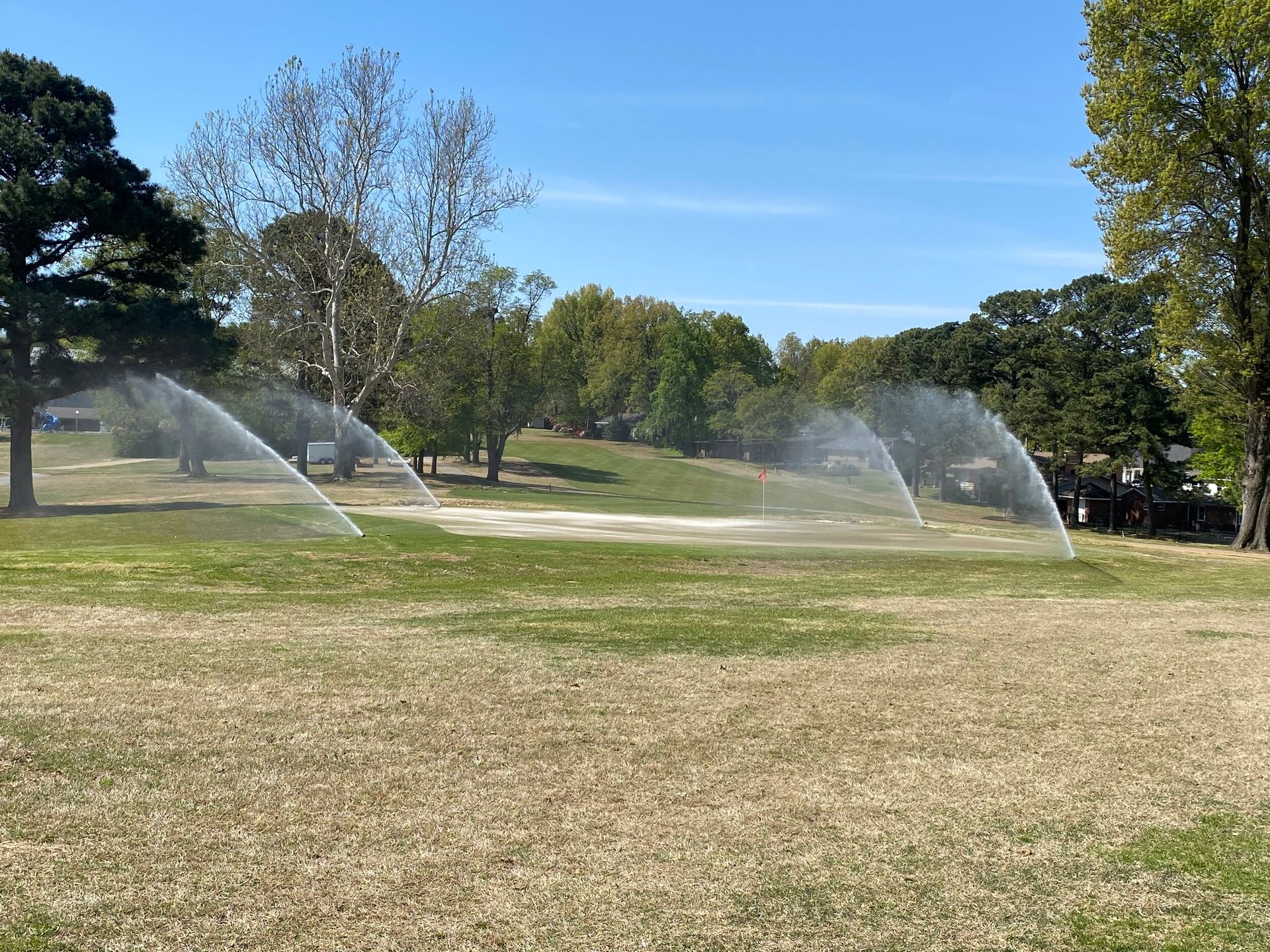 Sprinklers spraying water across a dry grassy park on a sunny day