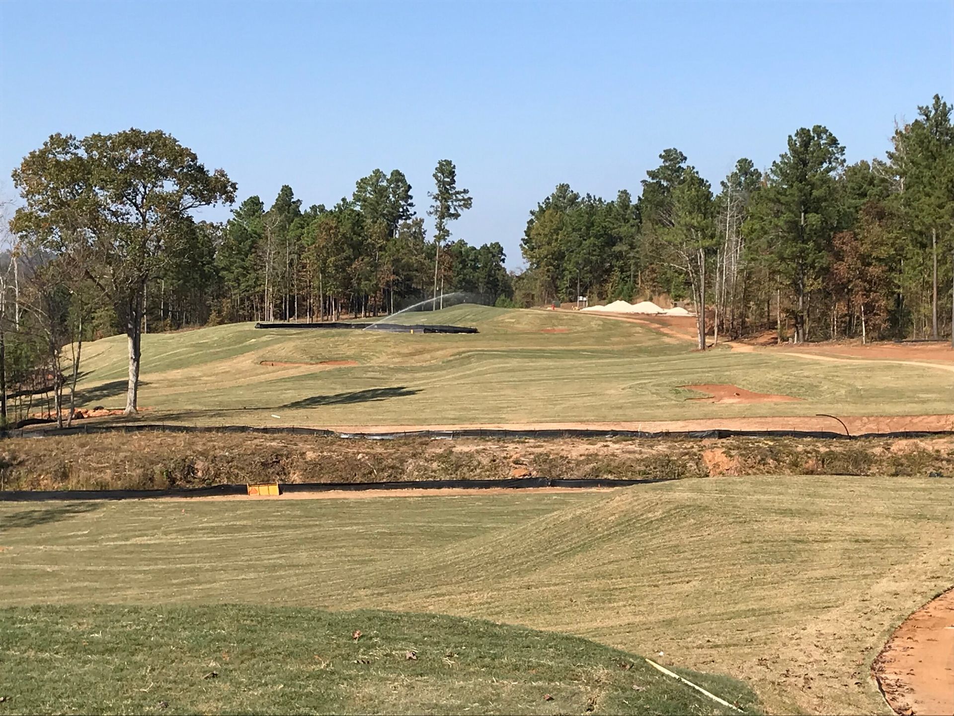 Golf course fairway with sand bunker, trees, and a blue sky
