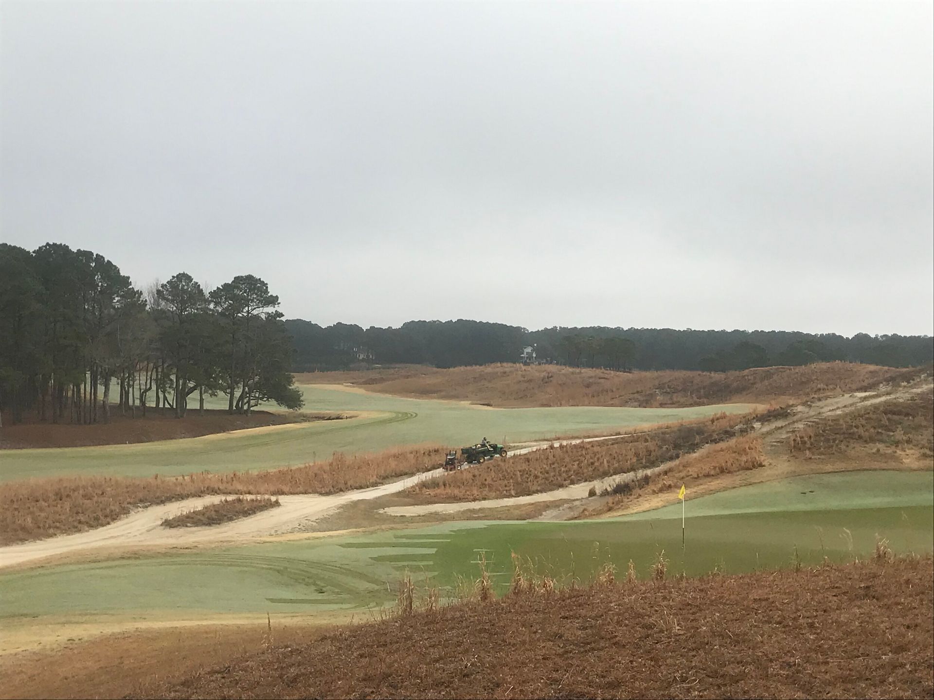 Sandy golf course with winding paths, green fairways, and trees under a cloudy sky