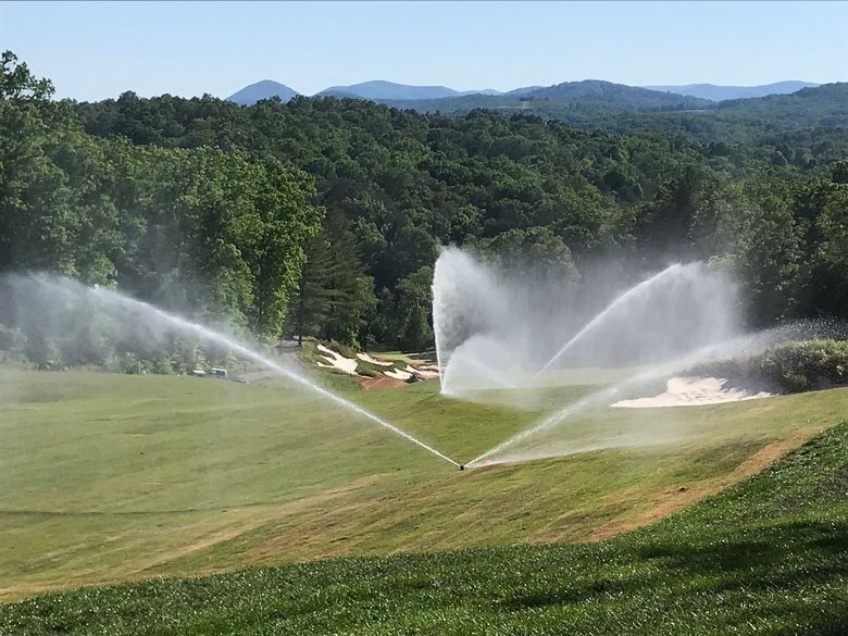 Sprinklers watering a green hillside with forested mountains in the background.