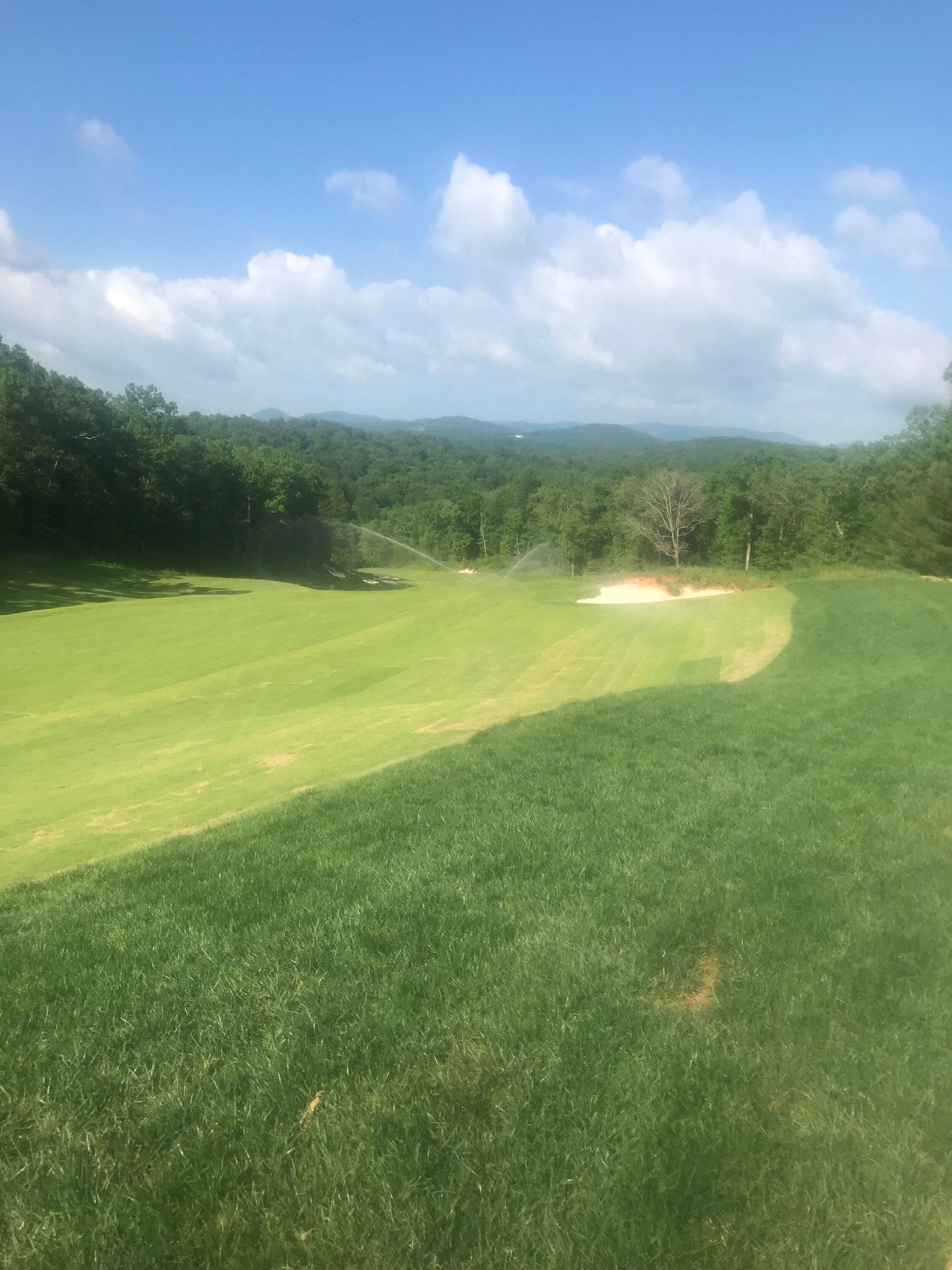 A green golf fairway with sand bunker under a blue sky with clouds