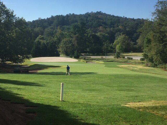 Golf course fairway with sand bunkers, a lone golfer, and wooded hills under a clear sky
