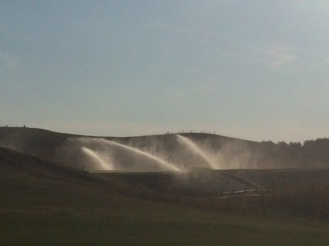 Irrigation sprinklers spraying water across a grassy field at sunset