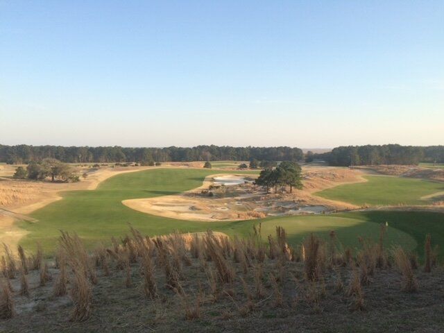Golf course fairway with sand bunkers and trees under a clear blue sky