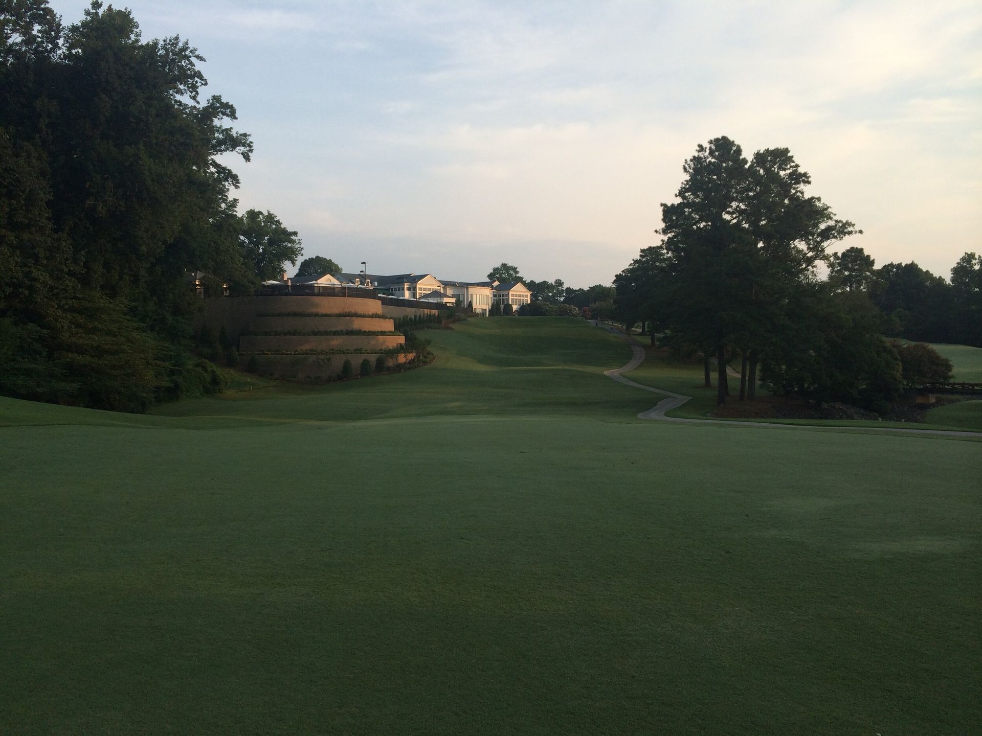 Golf course fairway at dusk with trees and distant clubhouse buildings