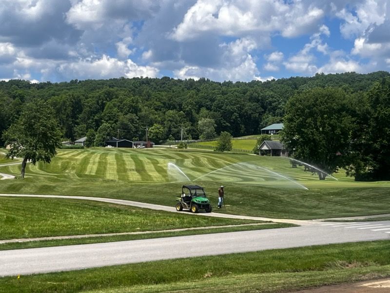 Golf course with striped fairway, a cart and two people near a road under a cloudy sky
