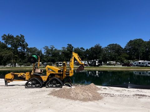 Yellow backhoe parked by a pond under a clear blue sky