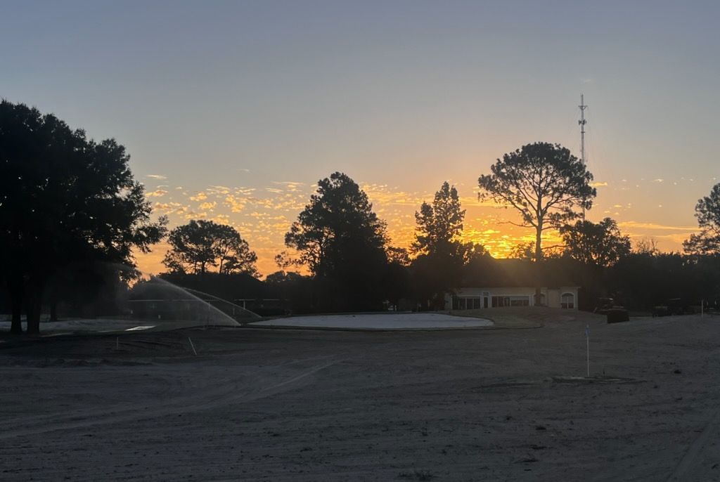Sunset over a dark field with silhouetted trees and a tall tower against a glowing sky