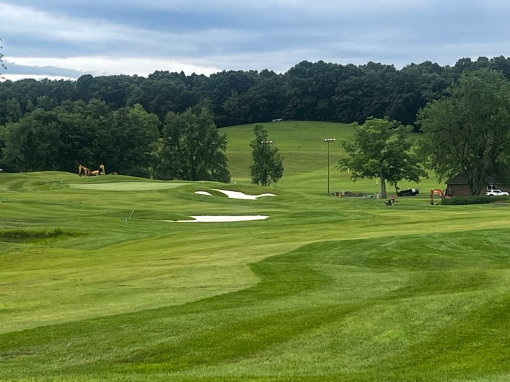 Green golf course with sand bunkers, rolling fairways, and trees under a cloudy sky