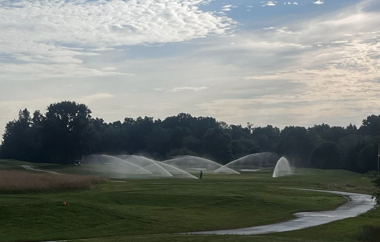 Golf course with sprinklers watering green fairway under a cloudy sky