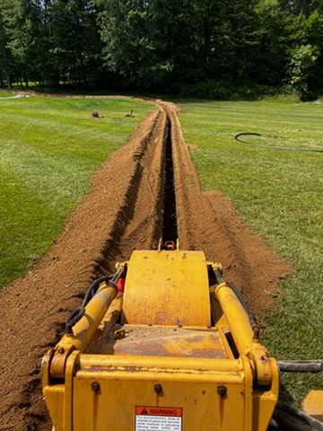 Yellow trenching machine cutting a long narrow trench across a grassy field