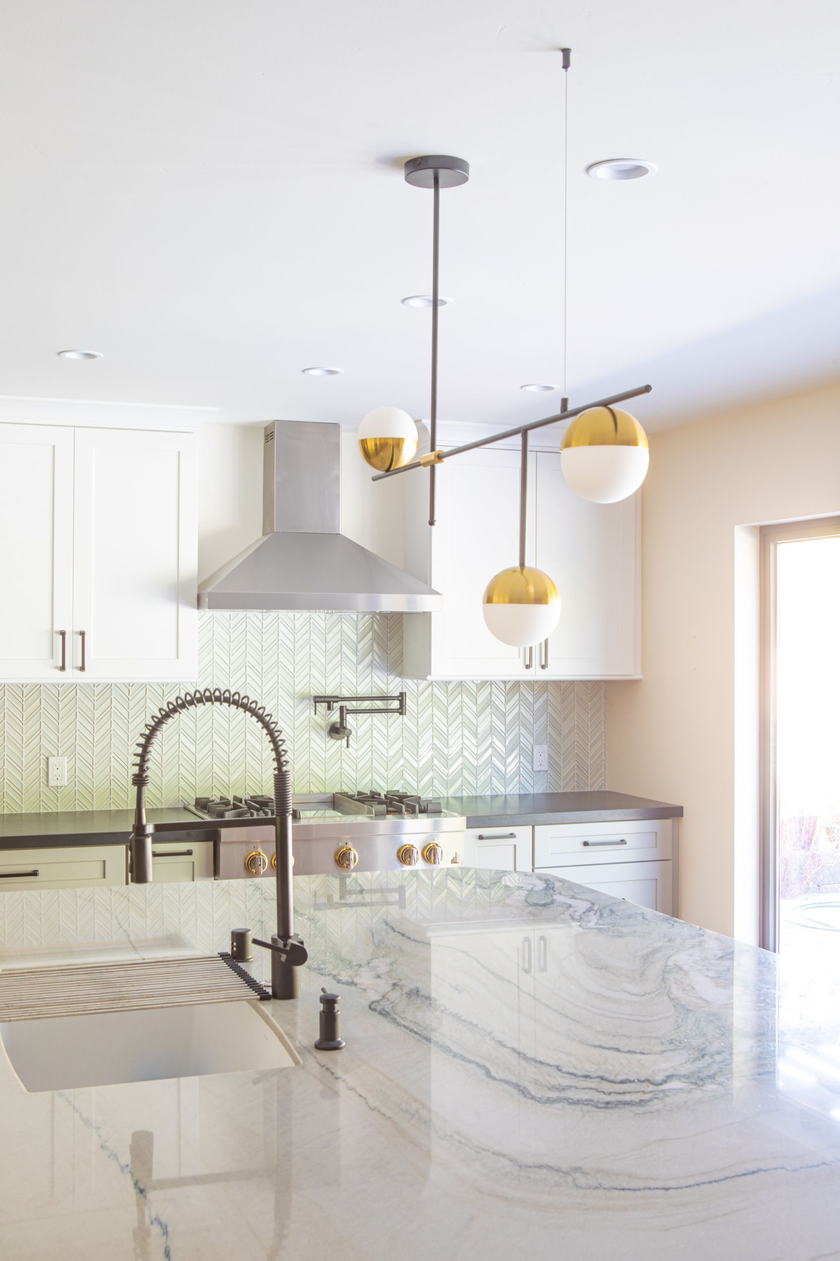 Modern kitchen with island, marble countertop, pendant lights, stainless steel range hood, and sink.