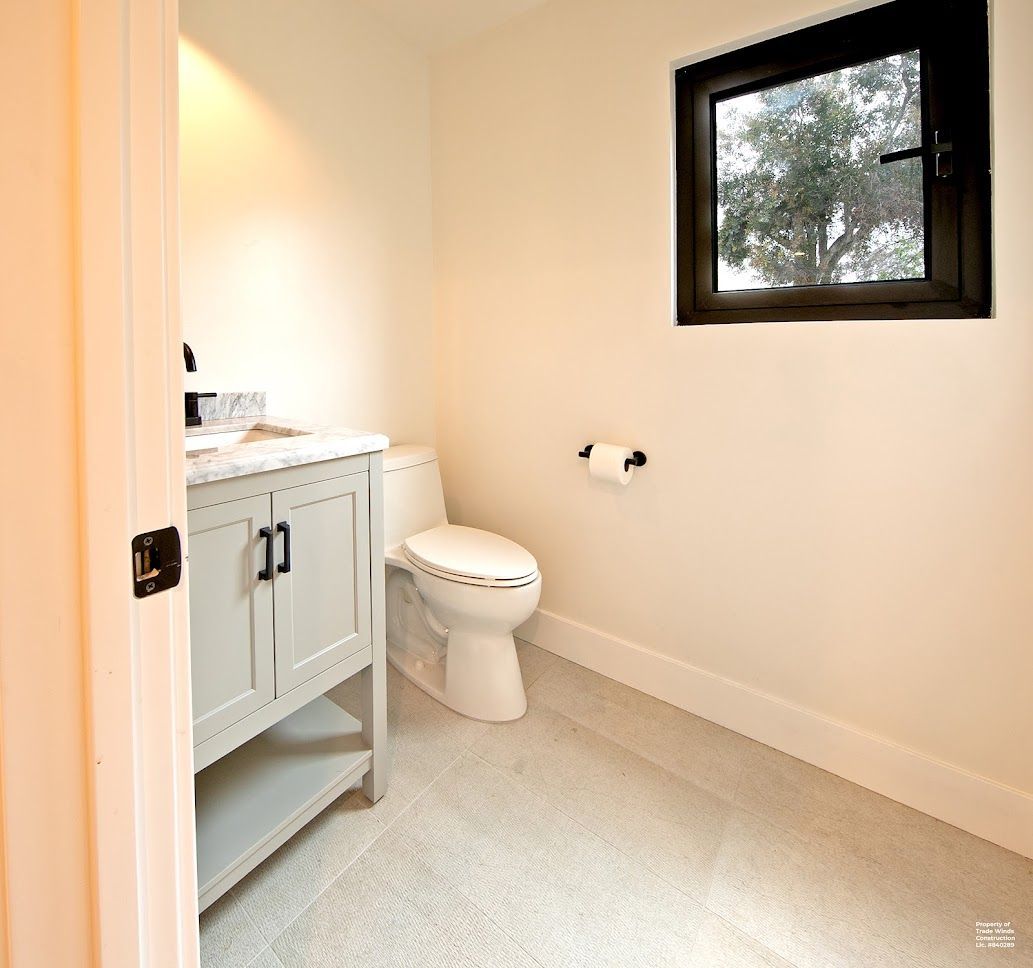 Powder room with a toilet, light blue vanity, small black window, and white walls.