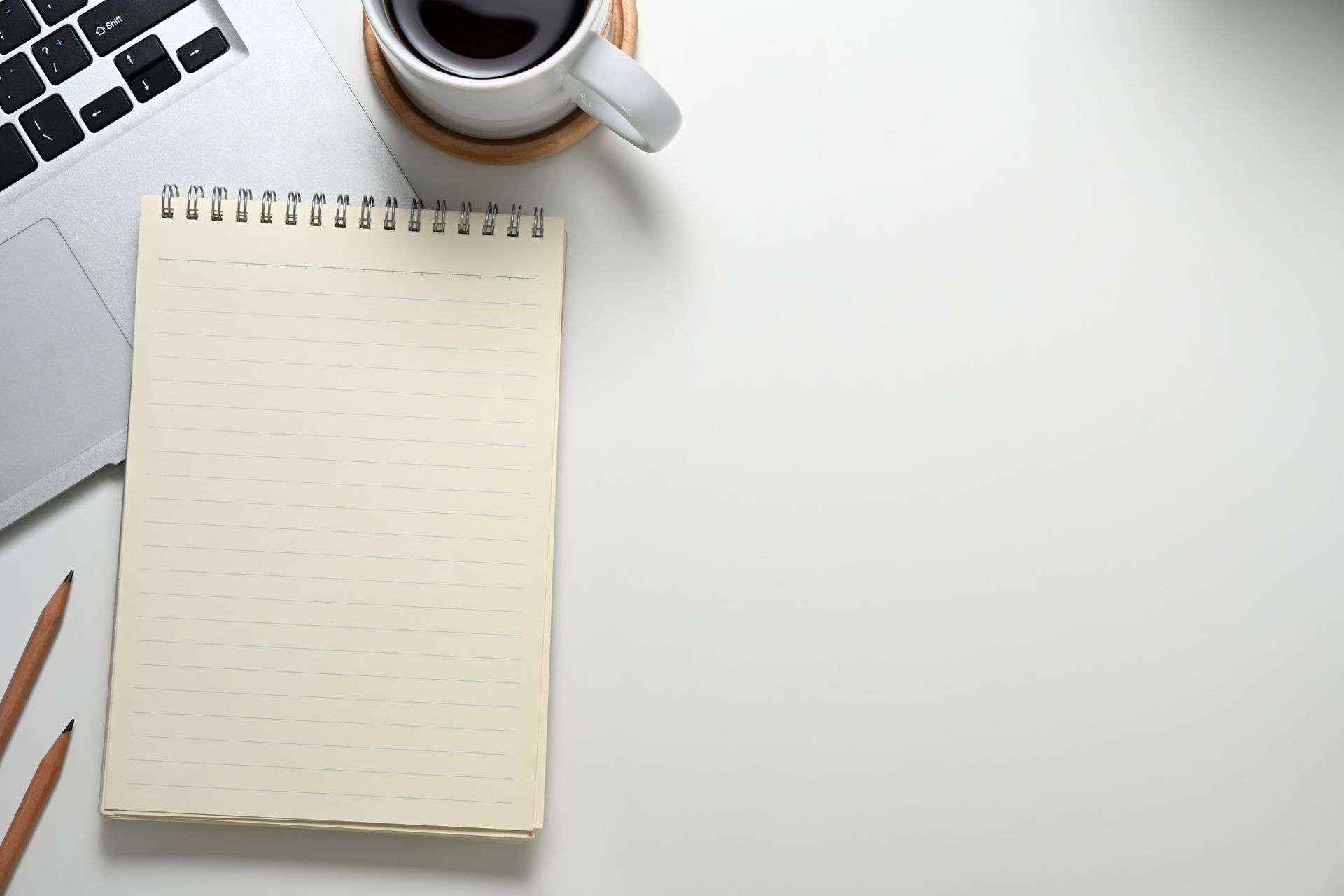 Laptop, notebook, pencils, and coffee cup on a white desk.