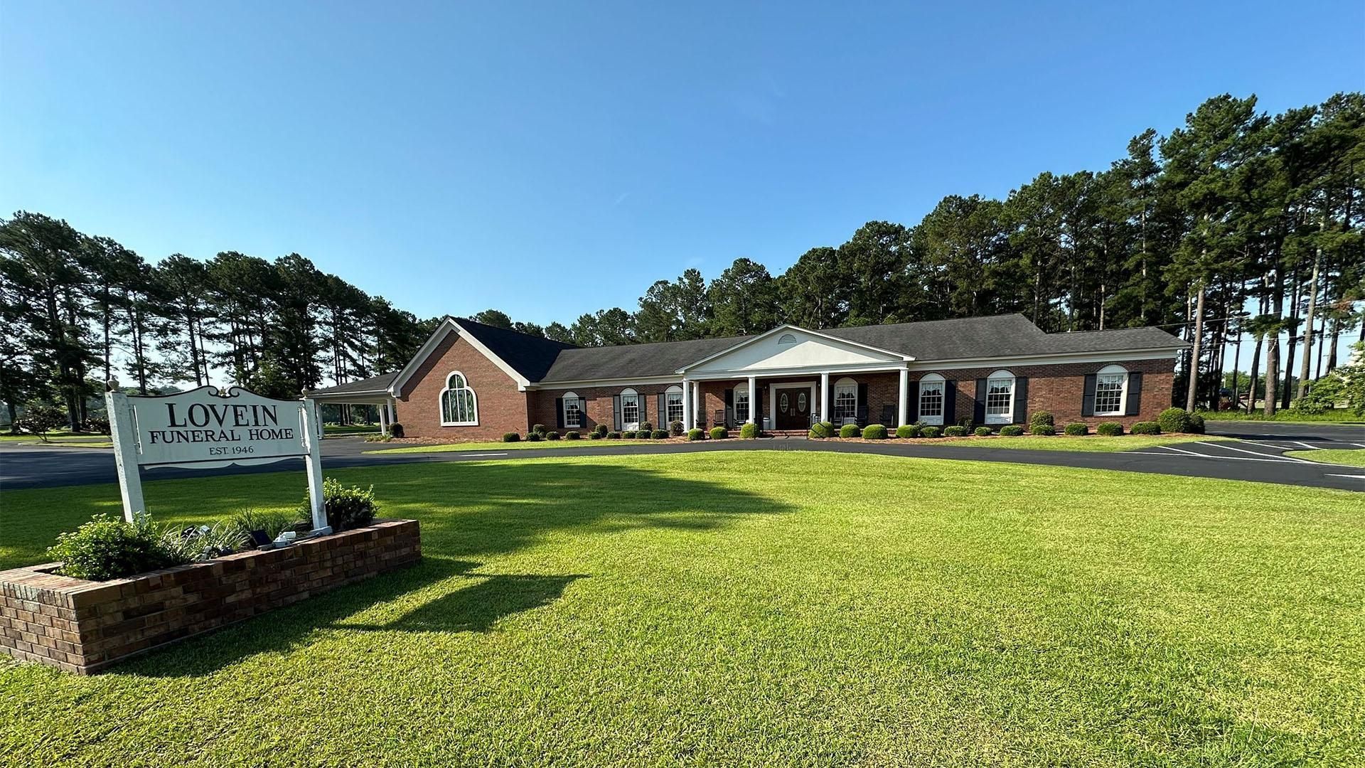 Lowman Funeral Home exterior, brick building with white columns and sign on lawn.