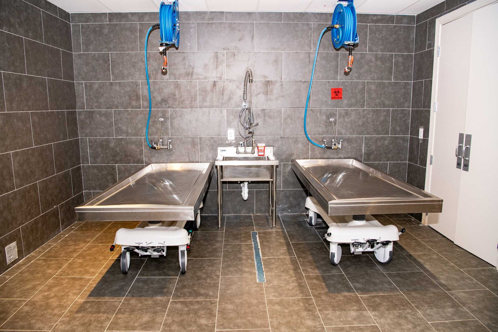 Animal shelter exam room with two stainless-steel tables, sinks, and blue overhead exam lamps