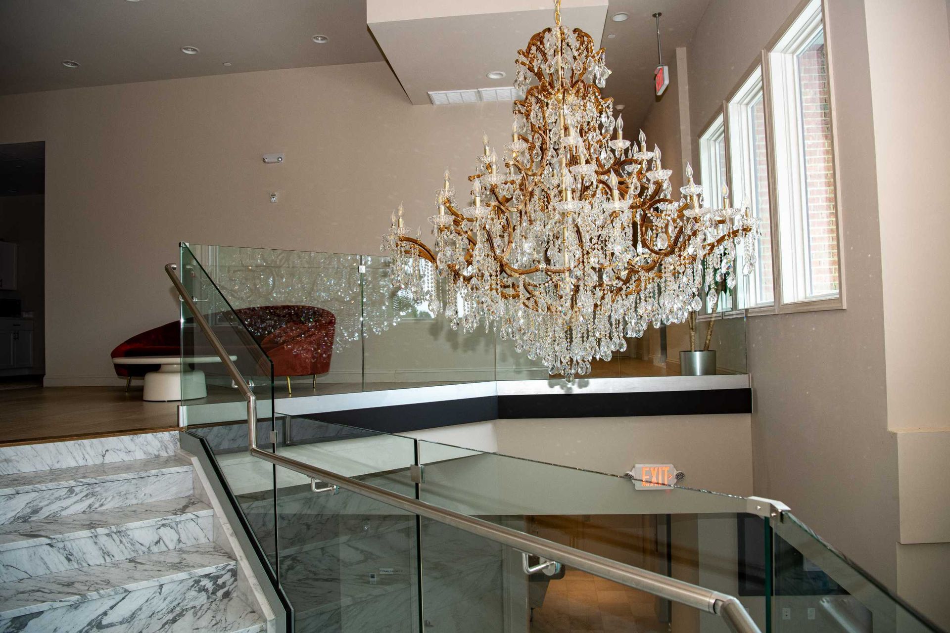 Modern staircase with glass railings and a large chandelier in a bright interior hall