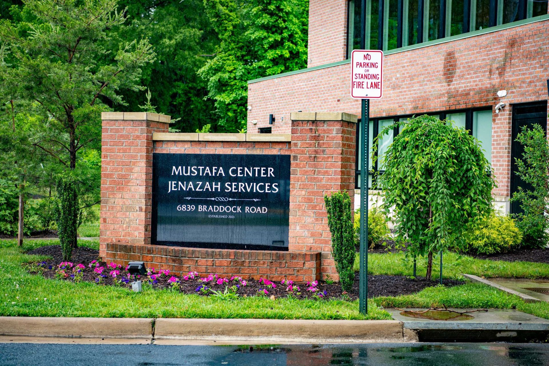 Brick sign for Mustafizur Center near Center City, with trees and a wet street in front