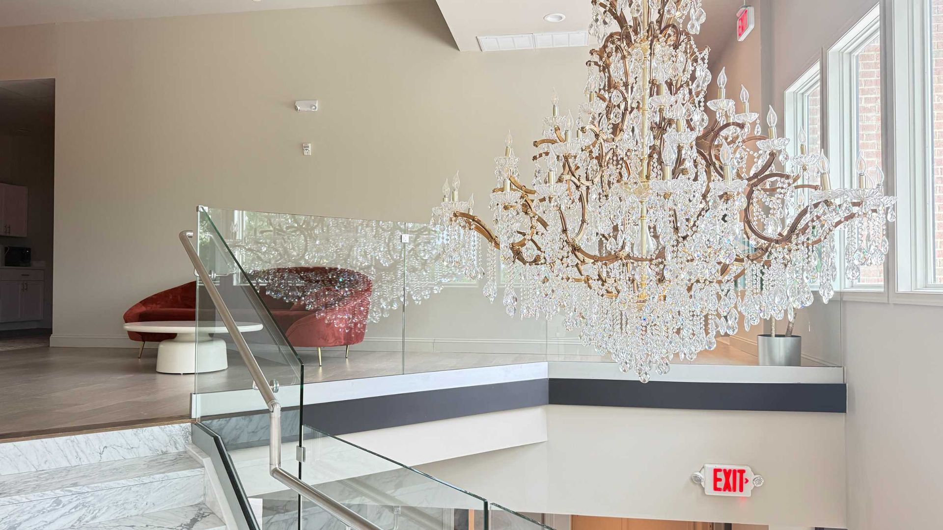 Elegant lobby with a large chandelier, glass railing, and modern seating near tall windows