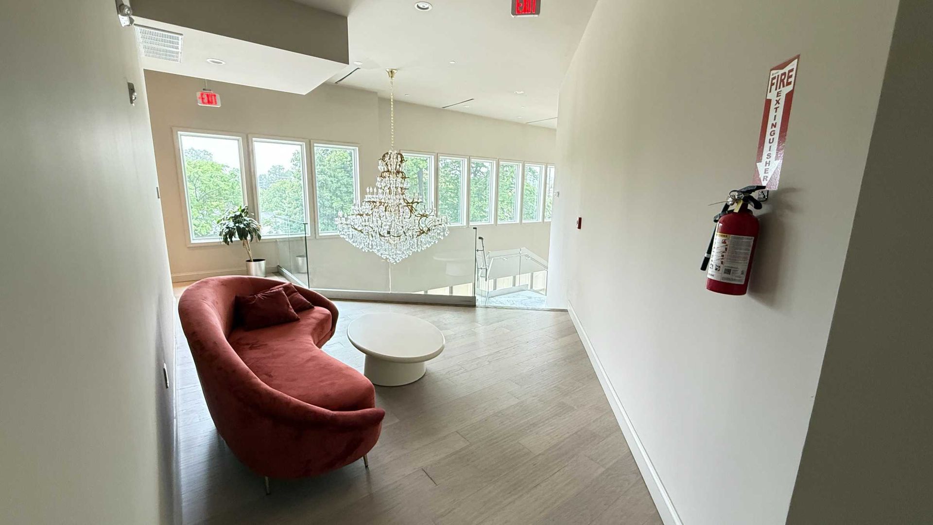 Modern lobby with a red sofa, white coffee table, large windows, and a wall-mounted fire extinguisher.