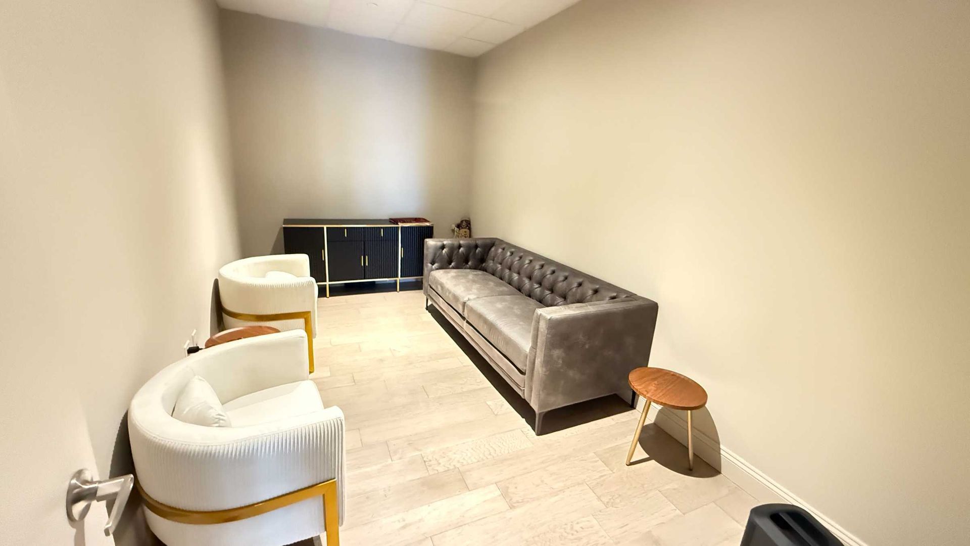 Minimalist beige living room with a gray sofa, white chairs, and a small wooden stool.
