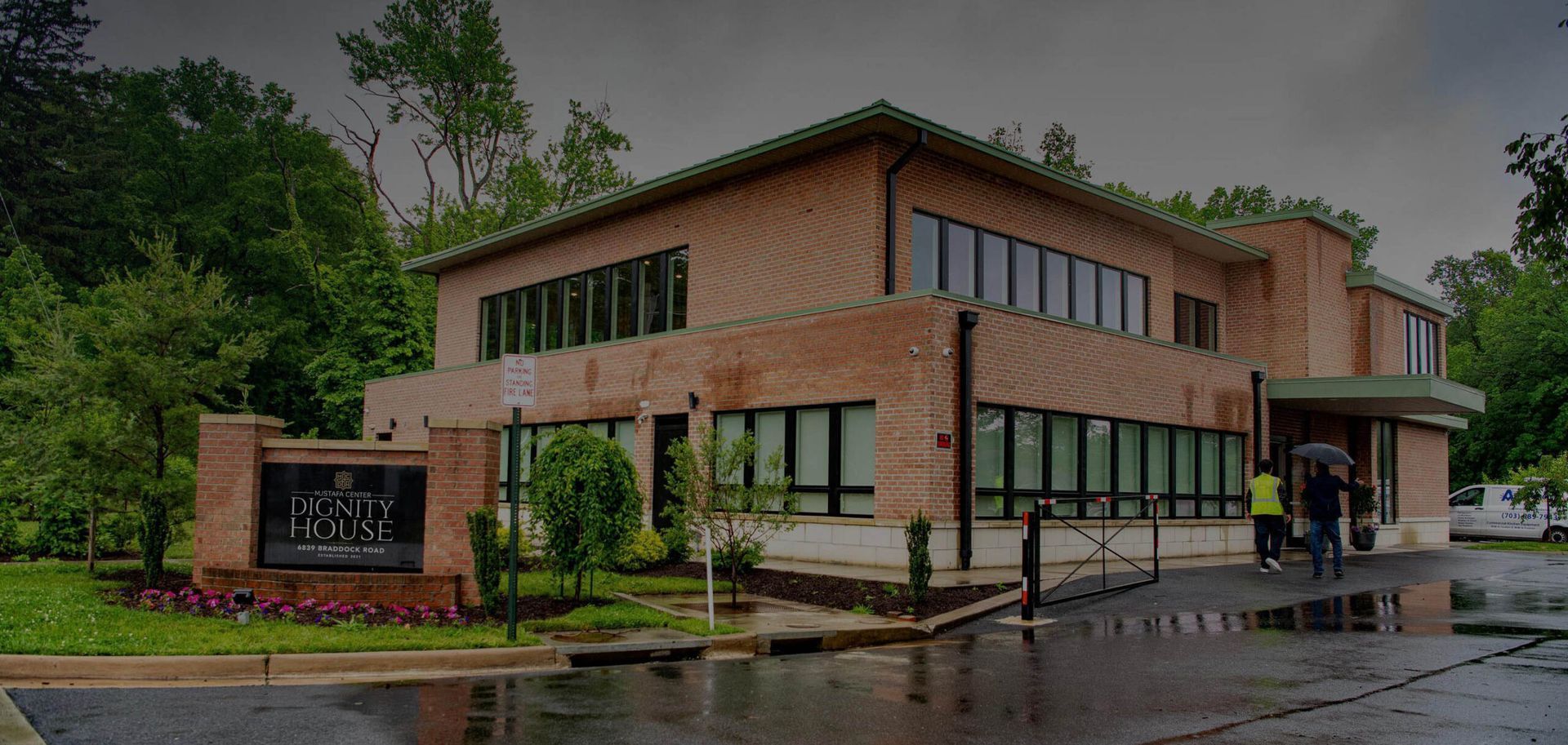Brick office building with large windows on a rainy day, surrounded by trees and wet pavement