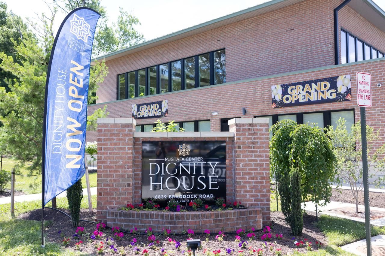 Brick building with Dignity House sign and a “Now Open” banner outside.