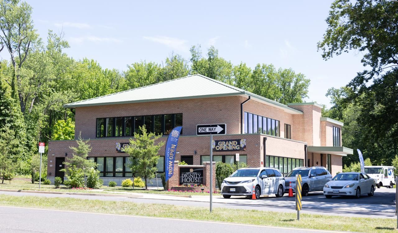Two-story brick office building with parked cars and trees along a road