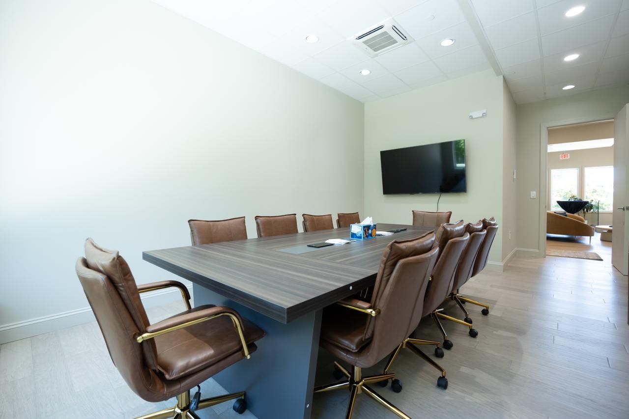 Modern conference room with long table, brown chairs, wall-mounted TV, and large windows