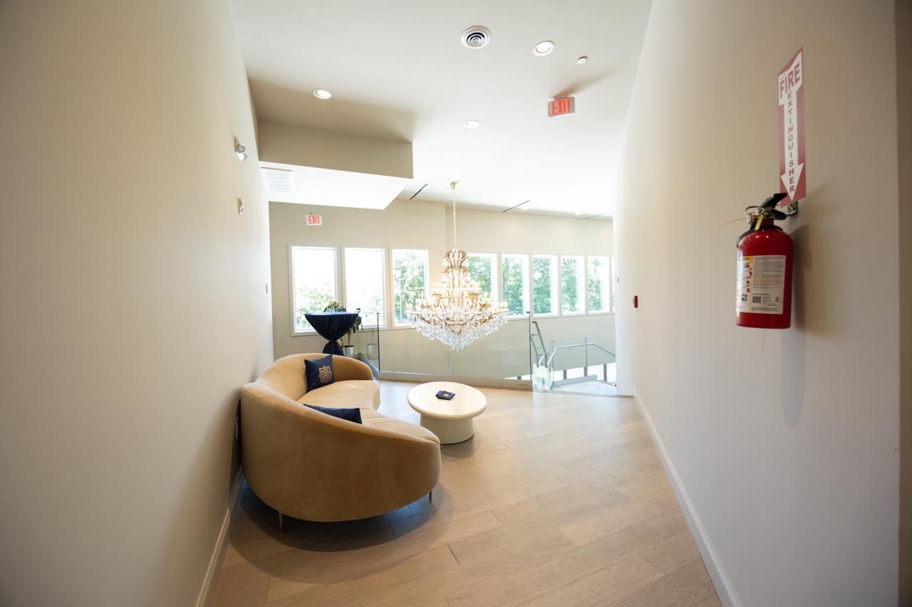 Bright lobby with tan seating, white tables, glass windows, and a red fire extinguisher on the wall