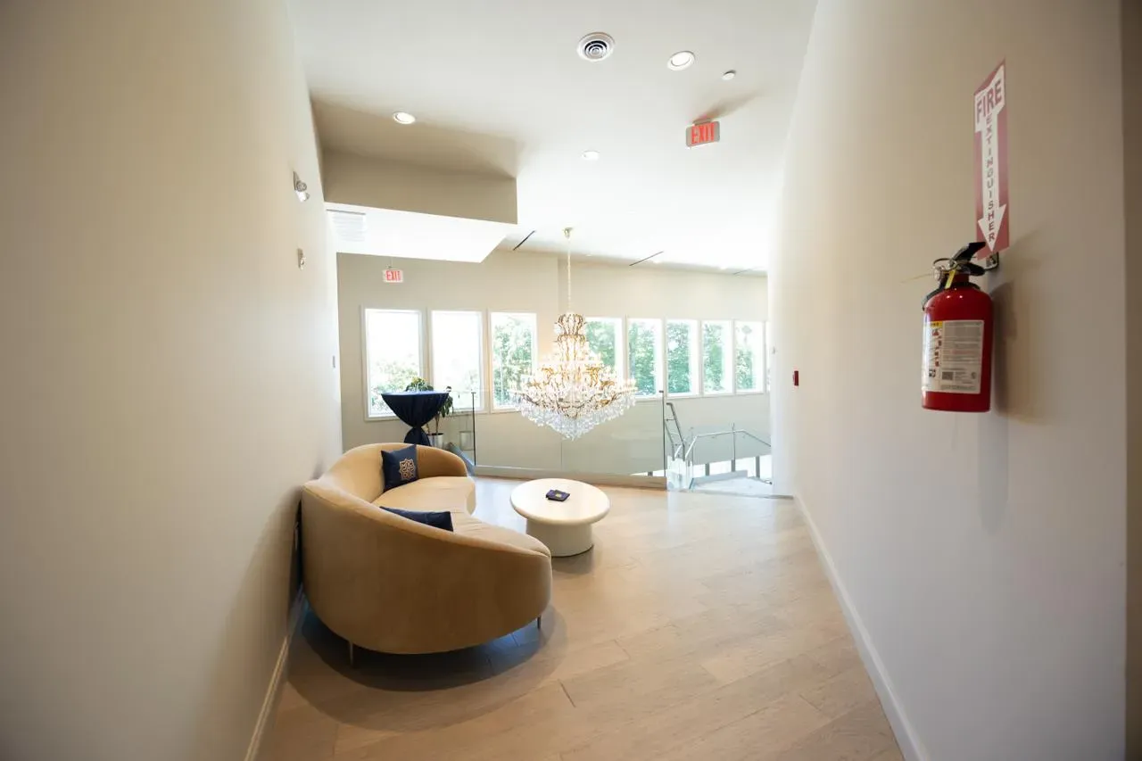 Modern lobby with tan chairs, round table, large windows, and a fire extinguisher on the wall