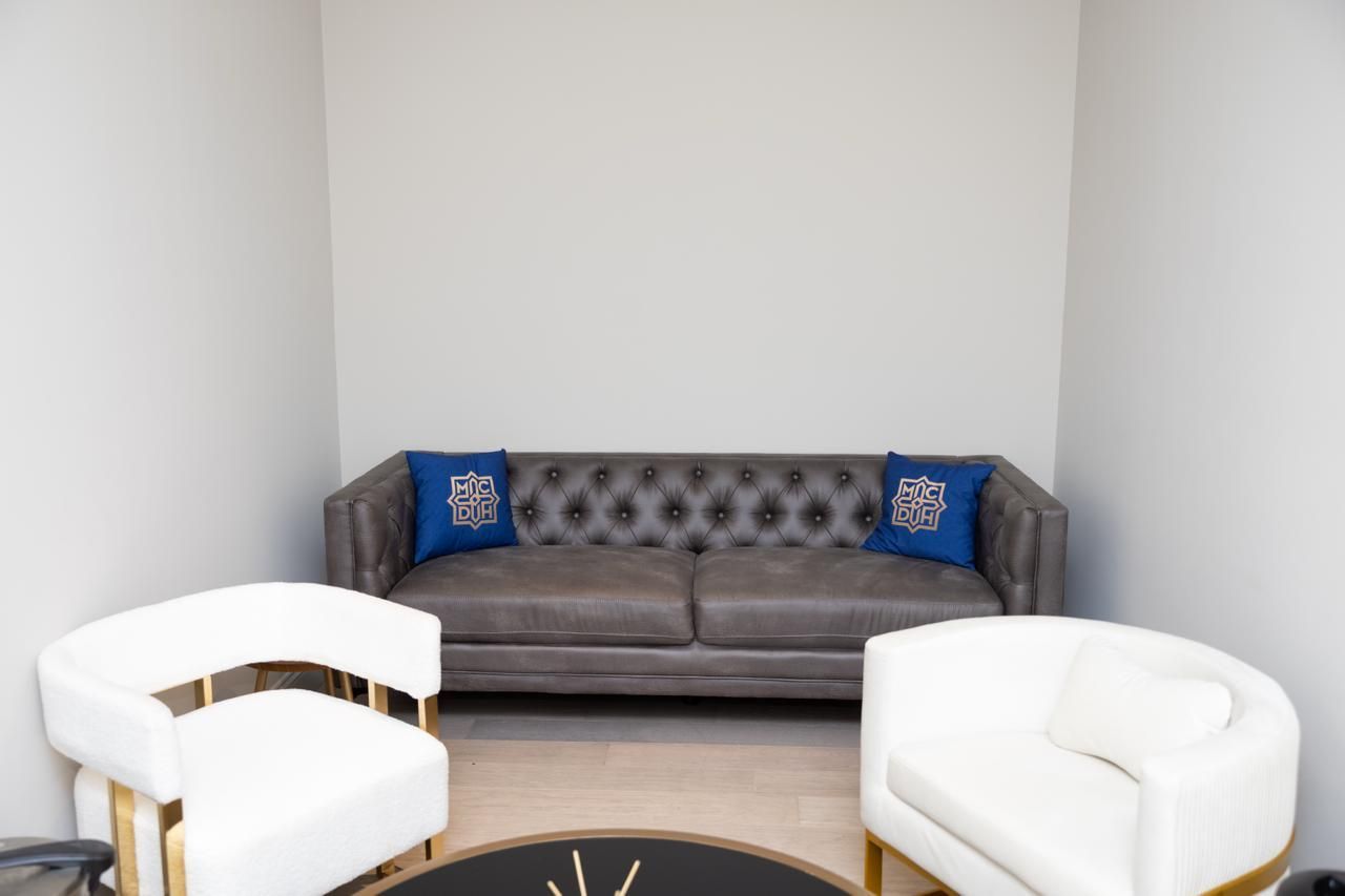 Modern lounge with gray tufted sofa, white chairs, and blue accent pillows in a bright alcove
