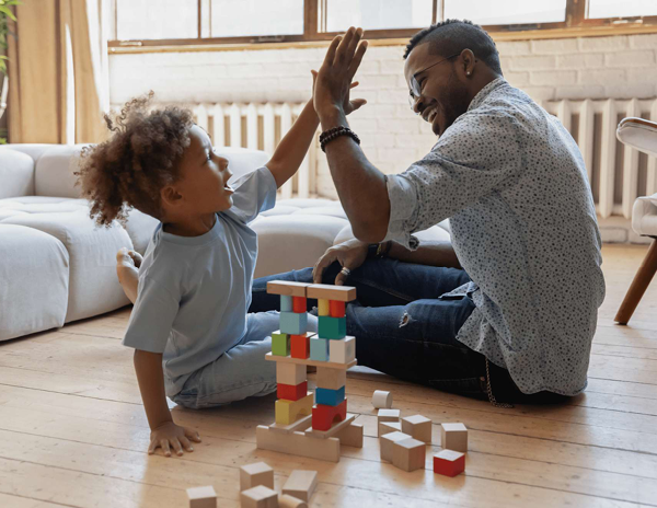 A man and a child sitting on the floor playing with wooden blocks