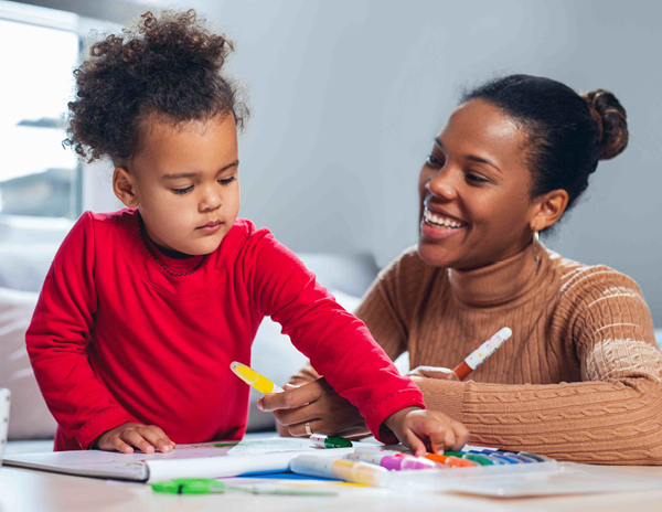 A woman and a child sitting at a table playing with markers 