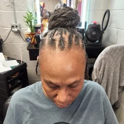 A woman with dreadlocks in a bun is wearing a blue shirt.