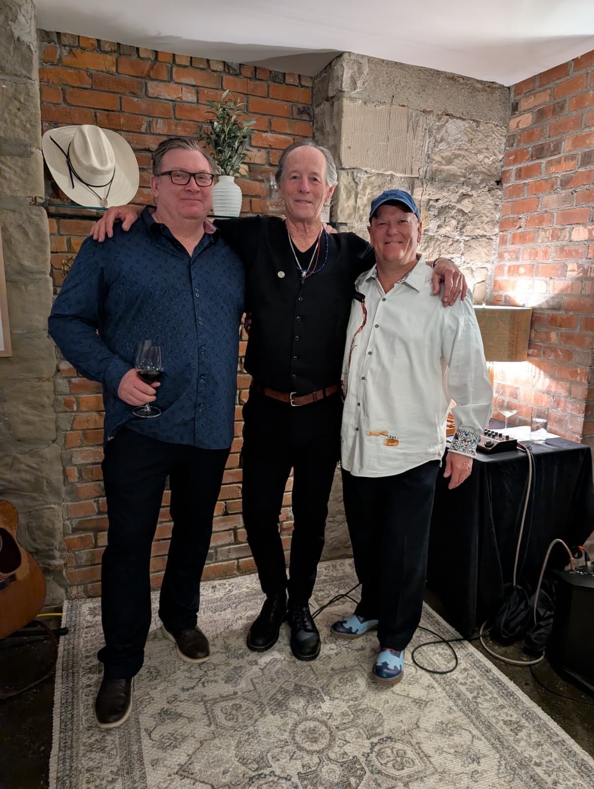 Four people posing indoors against a brick-and-stone wall, smiling in casual clothing.