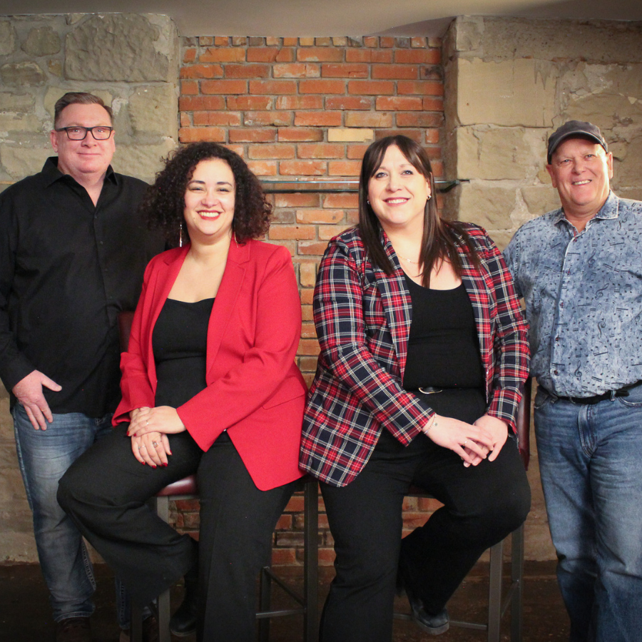 Four people posing indoors against a brick-and-stone wall, smiling in casual clothing.