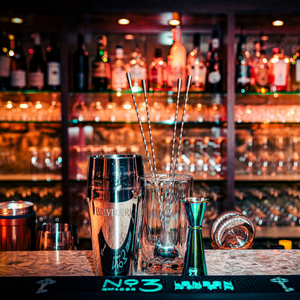 Bar counter with cocktail tools and glasses in a warmly lit, mirrored bar interior