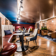 Modern lounge with brick walls, leather seating, round tables, and a glossy wood floor under warm lighting