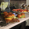 Assorted burgers and a fruit platter on a buffet counter in a kitchen or café setting