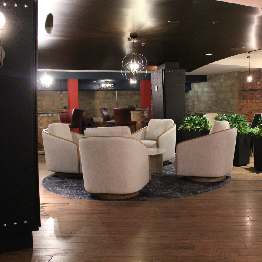 Modern lounge with cream chairs around a circular rug, wood floor, dark ceiling, stone walls, and red accents