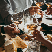 Friends toasting white wine and cheese at a cozy dinner table