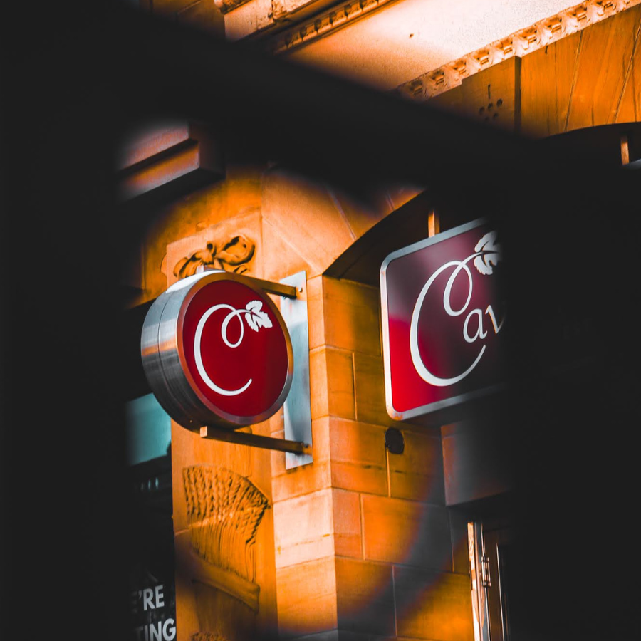 CavernUs signs on a warmly lit building at night, seen through a dark fence