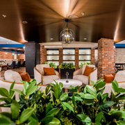 Stylish lounge with white chairs, orange pillows, brick columns, and green plants under warm lighting
