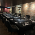 Elegant restaurant dining room with a long black table set for guests against brick walls and dim lighting