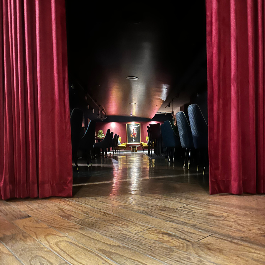 Red velvet curtains framing a dim auditorium with rows of chairs and a wooden floor